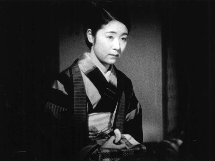 a Japanese woman in traditional dress seated with a somber expressionalr