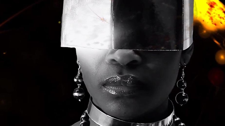 a black and white close-up of a Black woman wearing a silver mask over her eyesalr