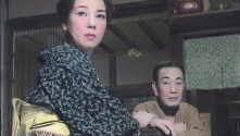 a Japanese man and woman in traditional dress look past the camera with concerned expressions