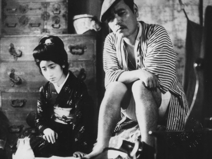 A woman in traditional Japanese dress and a man with a beret, sitting next to each other looking despondentalr