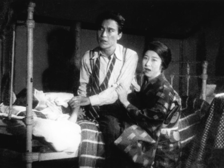a man and a woman sit on the edge of a child's bed looking offscreen, shockedalr