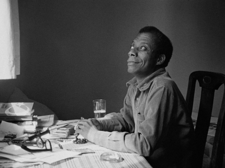James Baldwin at his desk looking up and smilingalr