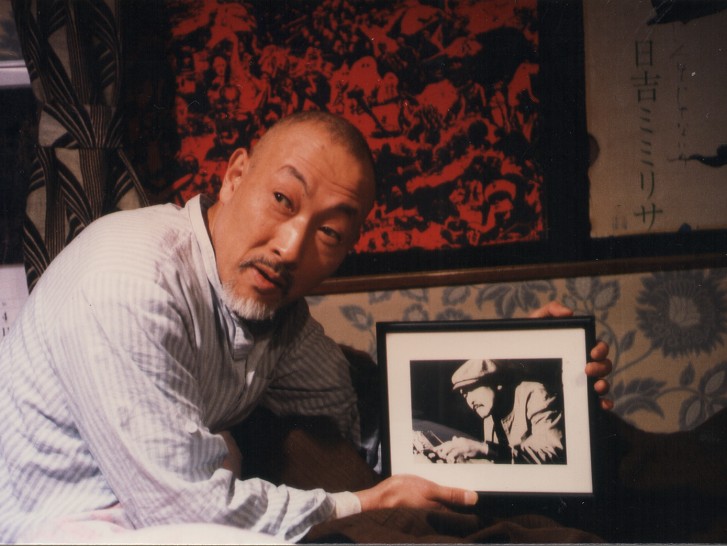 a Japanese man holds a black and white photo of another manalr