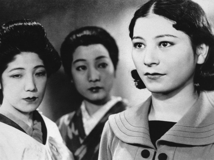 two young women stand next to a third who gazes expectantly off alr