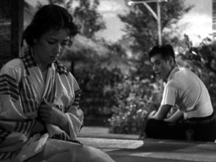 a young woman with her head down sits a distance away from the young man speaking to her outsidealr