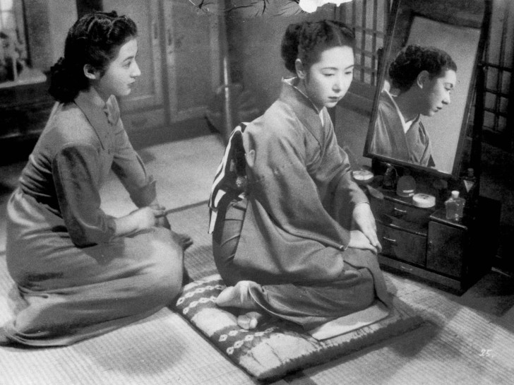  Tanaka Kinuyo seated before her mirror and makeup, looks away despondently, while a younger woman sits next to her looking eageralr