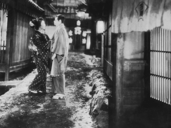 in this slightly faded photo, a Japanese couple talk in the narrow, wintery city streetalr