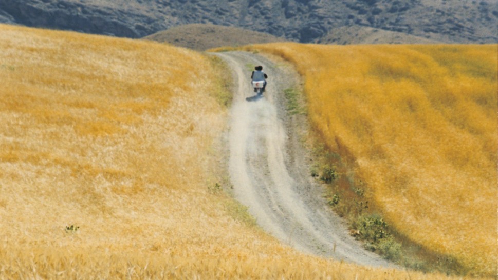 wide shot of a motorcycle driving on a winding road through the Iranian mountainsidealr