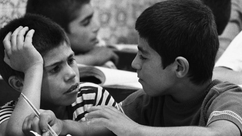 two boys in school talking at their deskalr