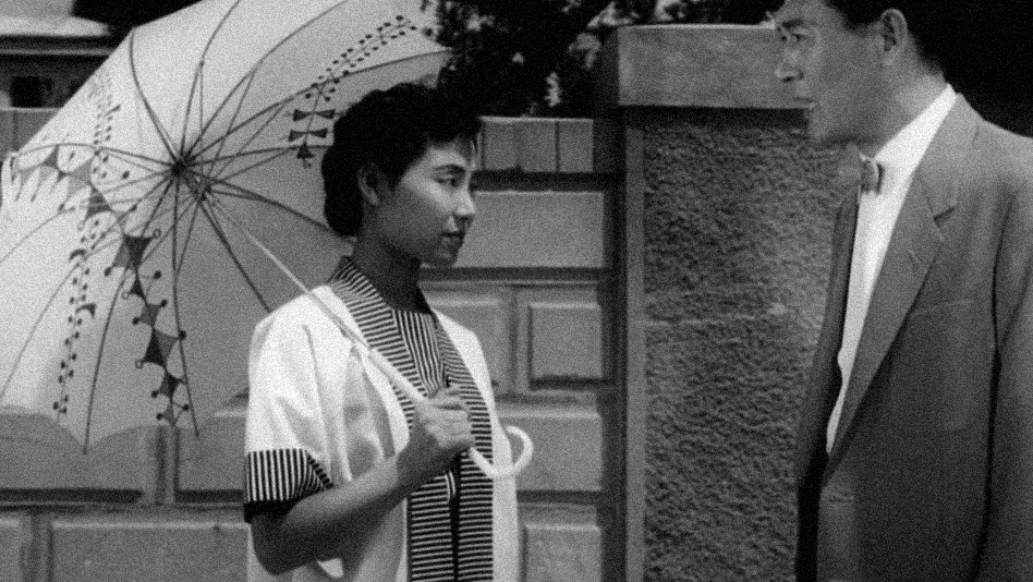 a Korean woman with a parasol talks to a Korean man in a suitalr