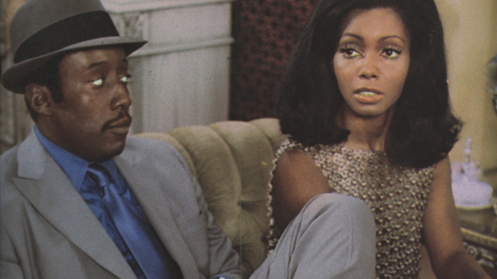 Godfrey Cambridge looking skeptically at Judy Pace who wears a metallic gold topalr