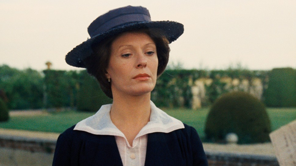 Delphine Seyrig as Aloïse in a hat, walking in a gardenalr