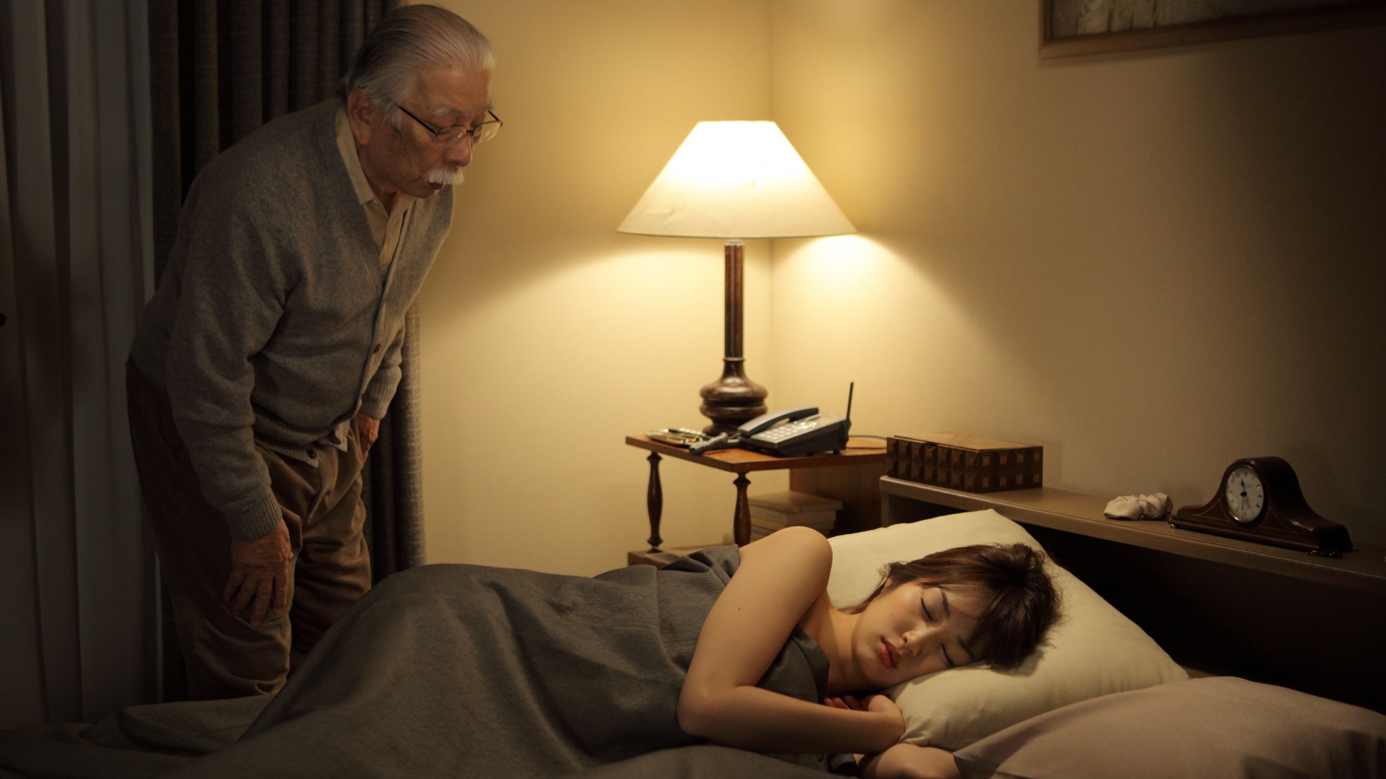 older man looking at a young woman asleep in a bed at nightalr.