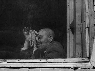 the black-and-white profile of a man holding a scarf up to his face and leaning against the window