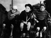 Three young boys sitting next to one another, looking off to the side, scowling