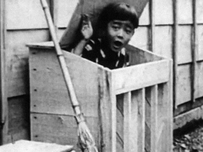 a young boy popping his head out of a wooden bin