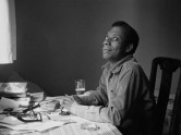 James Baldwin at his desk looking up and smiling