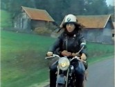 white man with long hair and a helmet rides a motorcycle through the countryside