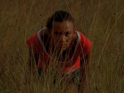 teenage Brazilian girl crouches in the tall grasses, looking at the camera