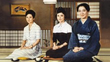 three Japanese women seated on mats with tea, one wearing traditional dress