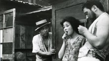 a black and white image of a Japanese man in a hat looking at two other disheveled people