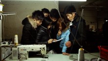 a group of young Chinese people gathered closely together in puffy coats, studying a document
