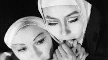 a close-up of two nuns' faces next to one another, one holding the other's hand to her mouth
