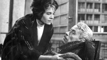 Delphine Seyrig leaning over an older man in a wheelchair