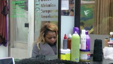 a Black woman with bleached, long hair is reflected in the mirror of a beauty parlor