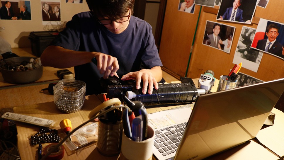 Tamoto Soran in front of a laptop and desk, putting together a homemade gunalr