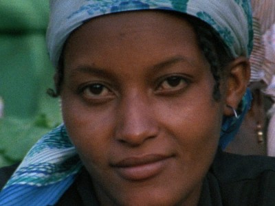 a close-up of a Bissau-Guinean woman wearing a scarf on her head and looking directly at the camera with a slight smile